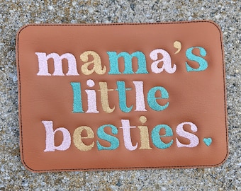 Könnte beinhalten: Ein braunes Lederstück mit dem Text "mama's little besties." in rosa, gold und türkis gestickt.