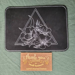 May include: Black mouse pad with white embroidered design of a crescent moon and flowers inside a triangle. A small thank you card with the text "Thank you for supporting my small business" and "Lauren's Assorted Creations" is in the foreground.