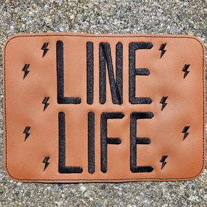 Peut inclure: Un patch en cuir marron avec du texte brodé noir qui dit "LINE LIFE" et est entouré d'éclairs noirs.