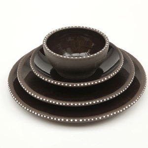 May include: A stack of dark brown ceramic dinnerware, including plates and a bowl. Each piece features a white dotted border. The glossy finish reflects light, highlighting the elegant design. This set is suitable for serving meals.