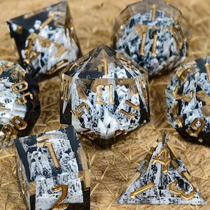 Peut inclure: Ensemble de sept dés polyédriques noirs, blancs et dorés. Les dés sont transparents avec un effet marbré et des chiffres dorés. Ces dés sont conçus pour les jeux de rôle sur table.