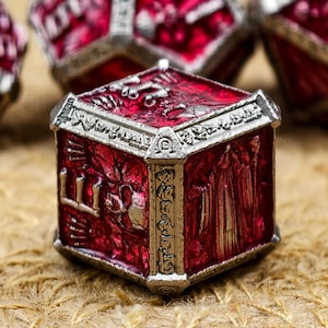 Puede incluir: Primer plano de un dado rojo y plateado. El dado tiene diseños y patrones intrincados en cada cara, con un borde plateado metálico. El dado está sobre una superficie texturizada y marrón.