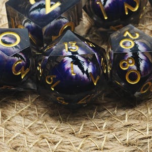 Peut inclure: Ensemble de dés polyédriques en résine transparente foncée. Chaque dé présente un motif violet et blanc avec des chiffres dorés. Ces dés sont conçus pour les jeux de société et les jeux de rôle.
