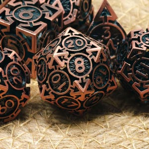 May include: Close-up of a set of copper-colored polyhedral dice. The dice have intricate designs with black detailing and are arranged on a textured, tan surface. The dice are used for tabletop games.