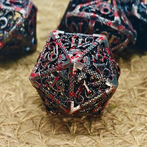 May include: Close-up of a set of polyhedral dice with a metallic, filigree design. The dice are primarily silver and black, with red accents. The numbers are clearly visible, and the overall aesthetic is gothic.