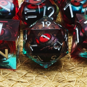 May include: A set of polyhedral dice with clear sides and red, black, and teal accents. Each die has white numbering. The interior of the dice has a red and black design. The dice are for tabletop games.