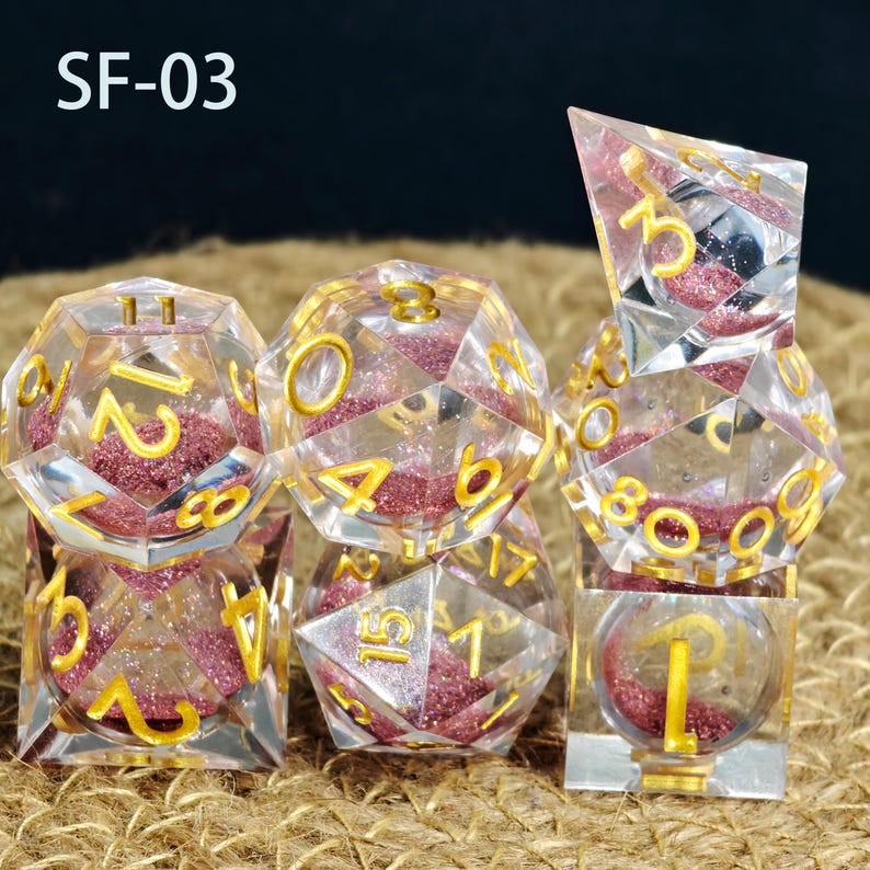 May include: A collection of clear, multi-faceted dice with gold numerals and pink glitter filling. The dice are displayed on a textured surface. The text "SF-03" is visible in the top left corner.