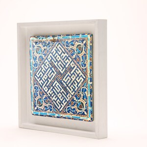 Peut inclure: Un carreau de c&eacute;ramique encadr&eacute; avec un motif g&eacute;om&eacute;trique bleu et blanc. Le carreau pr&eacute;sente une calligraphie arabe complexe et des motifs floraux.