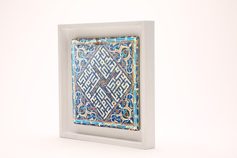 Peut inclure: Un carreau de c&eacute;ramique encadr&eacute; avec un motif g&eacute;om&eacute;trique bleu et blanc. Le carreau pr&eacute;sente une calligraphie arabe complexe et des motifs floraux.