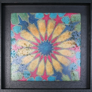 May include: A framed artwork featuring a colorful geometric pattern with a central star shape. The pattern is made up of red, blue, yellow, and green hues, creating a vibrant and intricate design.