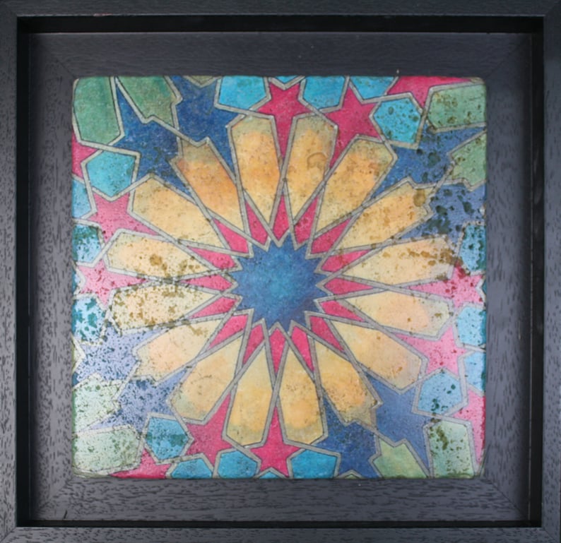 May include: A framed artwork featuring a colorful geometric pattern with a central star shape. The pattern is made up of red, blue, yellow, and green hues, creating a vibrant and intricate design.