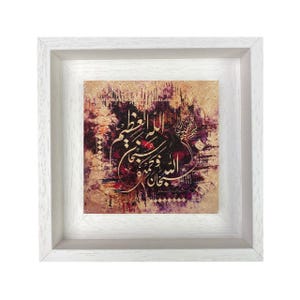 May include: A square wall art piece featuring gold Arabic calligraphy centred on a textured background of deep purple, brown, and cream tones. The artwork is encased in a white wooden frame with a visible grain, creating a clean border.