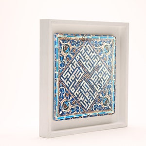 Peut inclure: Un carreau de c&eacute;ramique encadr&eacute; avec des motifs g&eacute;om&eacute;triques bleus et blancs complexes et de la calligraphie arabe. Le carreau est plac&eacute; sur un fond blanc.
