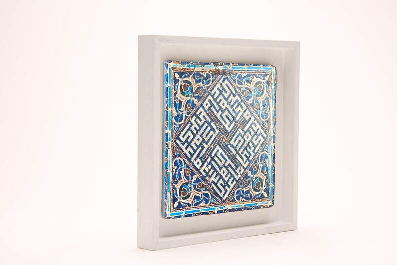 Peut inclure: Un carreau de c&eacute;ramique encadr&eacute; avec des motifs g&eacute;om&eacute;triques bleus et blancs complexes et de la calligraphie arabe. Le carreau est plac&eacute; sur un fond blanc.