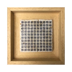 May include: A framed artwork with a beige background and a pattern of black squares. The artwork is in a light wood frame.