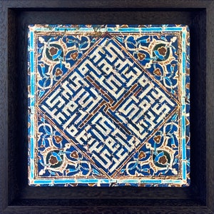 Peut inclure: Un carreau de c&eacute;ramique encadr&eacute; avec un motif g&eacute;om&eacute;trique bleu et blanc. Le carreau pr&eacute;sente une calligraphie arabe complexe en forme de losange, entour&eacute;e de motifs floraux.