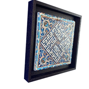 Peut inclure: Un carreau de c&eacute;ramique encadr&eacute; avec un motif g&eacute;om&eacute;trique bleu et blanc. Le carreau pr&eacute;sente des motifs complexes et de la calligraphie arabe.
