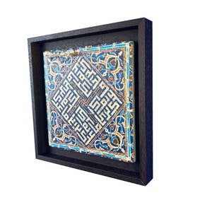 Peut inclure: Un carreau encadr&eacute; avec des motifs g&eacute;om&eacute;triques bleus et blancs complexes et des motifs floraux. Le carreau est plac&eacute; sur un fond brun fonc&eacute;.