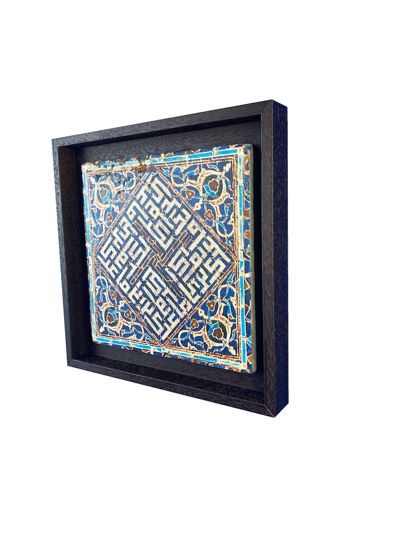 Peut inclure: Un carreau encadr&eacute; avec des motifs g&eacute;om&eacute;triques bleus et blancs complexes et des motifs floraux. Le carreau est plac&eacute; sur un fond brun fonc&eacute;.