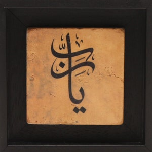 May include: A framed tile with black calligraphy on a tan background. The calligraphy is in Arabic script and reads "Allah".