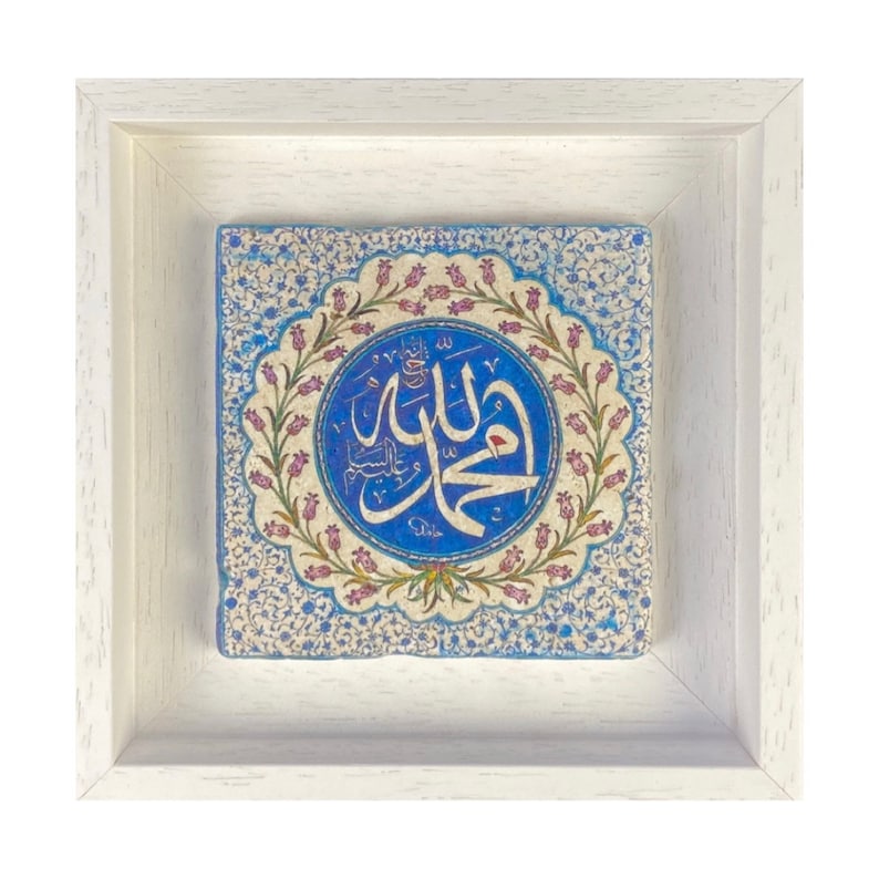 May include: Square framed artwork featuring Islamic calligraphy in blue and white. The central design is a blue circle with white script, surrounded by a floral border of pink and green. The frame is white.