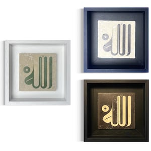 Op de afbeelding: Drie ingelijste vierkante kunstwerken. Elk heeft een getegelde tegel met Arabische kalligrafie in verschillende kleuren: groen, wit en geel. De frames zijn wit, marineblauw en zwart. De kunstwerken worden tegen een witte achtergrond gepresenteerd.