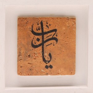 May include: A framed tile with black Arabic calligraphy on a tan background.