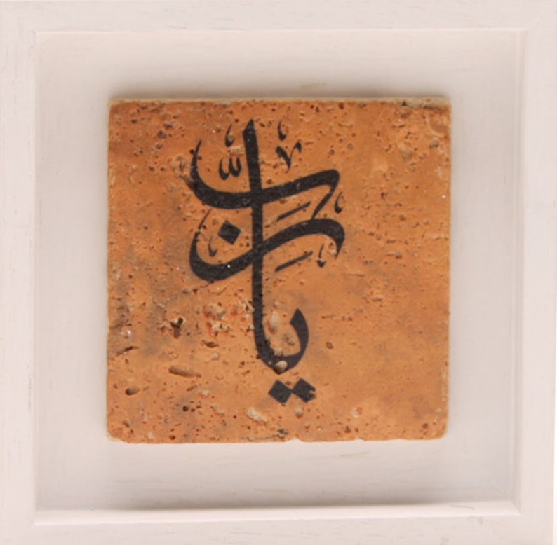 May include: A framed tile with black Arabic calligraphy on a tan background.