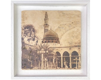 May include: A framed sepia-toned photograph of a mosque with a tall minaret and a domed roof. The mosque is surrounded by palm trees and other buildings. The photograph is framed in a white frame.