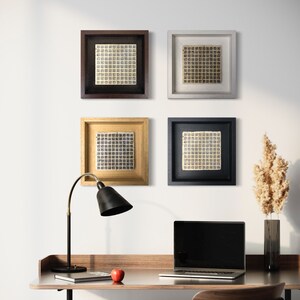 May include: Four framed square prints with a geometric pattern in black and white, hanging on a white wall. A black desk lamp with a black shade is on a wooden desk with a laptop computer, a book, and an apple.