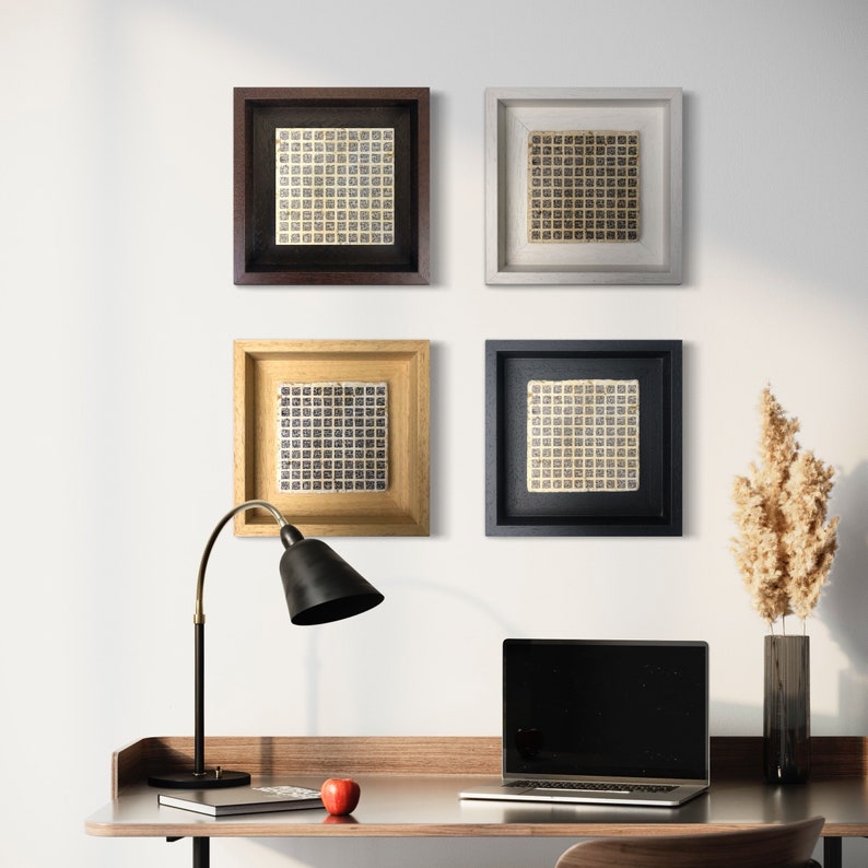 May include: Four framed square prints with a geometric pattern in black and white, hanging on a white wall. A black desk lamp with a black shade is on a wooden desk with a laptop computer, a book, and an apple.