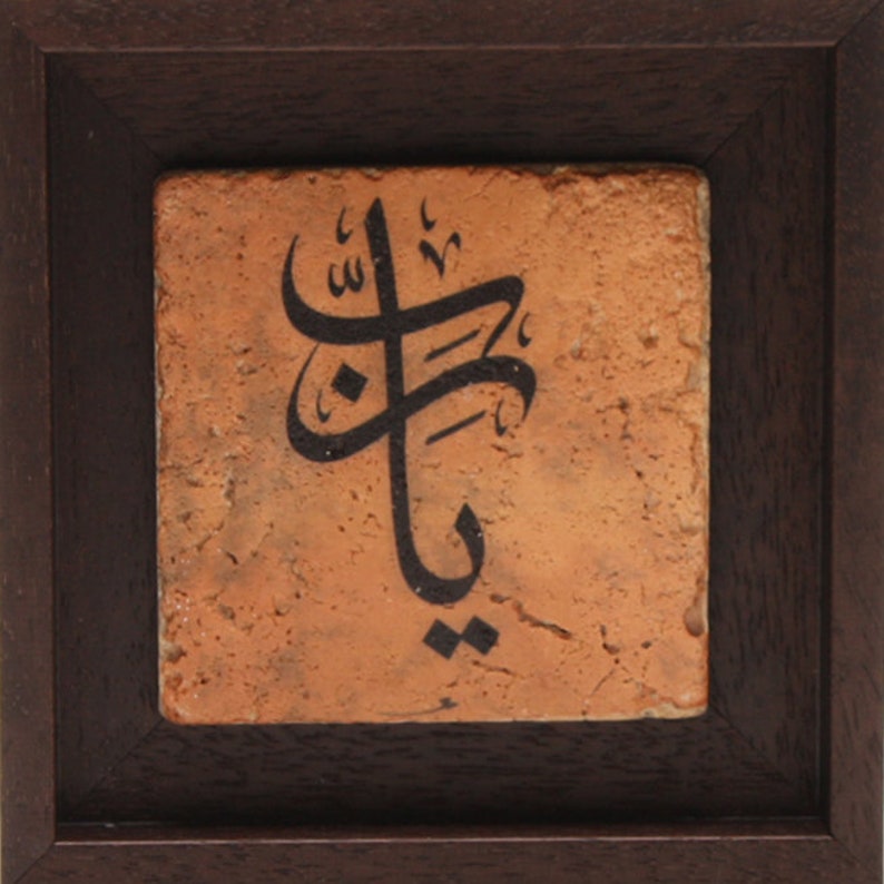 May include: A framed terracotta tile with black Arabic calligraphy. The tile is set in a dark wood frame.