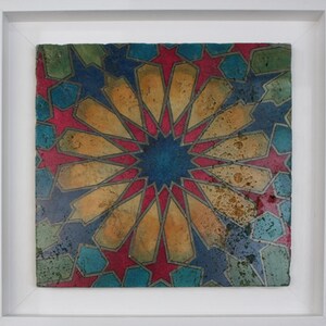 May include: A framed ceramic tile with a geometric pattern in shades of blue, red, gold, and green. The design features a central starburst with radiating lines and intricate details.