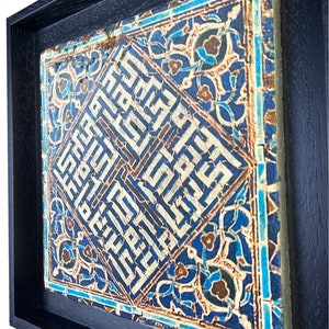 Peut inclure: Un carreau encadr&eacute; avec des motifs g&eacute;om&eacute;triques bleus et blancs complexes et de la calligraphie arabe. Le carreau est sur un fond bleu fonc&eacute;.