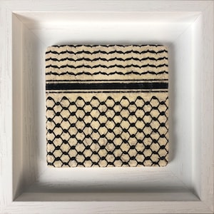Op de afbeelding: Een ingelijst kunstwerk met een zwart-witte gepatroneerde stof met een geometrisch ontwerp. De stof is gemonteerd op een witte achtergrond en ingelijst in een wit frame.