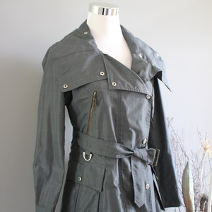 May include: A gray, long-sleeved, belted trench coat with a zipper and buttons. The coat has a collar that can be worn up or down.