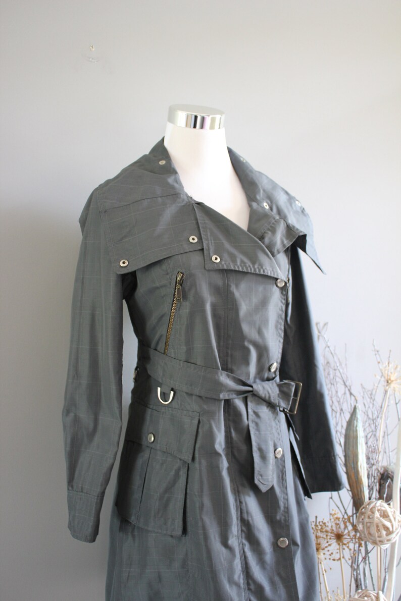 May include: A gray, long-sleeved, belted trench coat with a zipper and buttons. The coat has a collar that can be worn up or down.