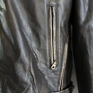 K&ouml;nnte beinhalten: Nahaufnahme einer schwarzen Lederjacke mit Rei&szlig;verschlusstasche und G&uuml;rteldetail.