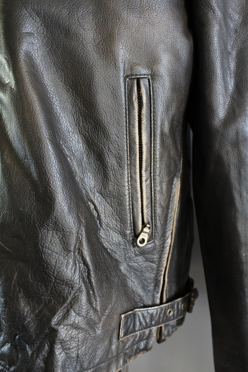 K&ouml;nnte beinhalten: Nahaufnahme einer schwarzen Lederjacke mit Rei&szlig;verschlusstasche und G&uuml;rteldetail.
