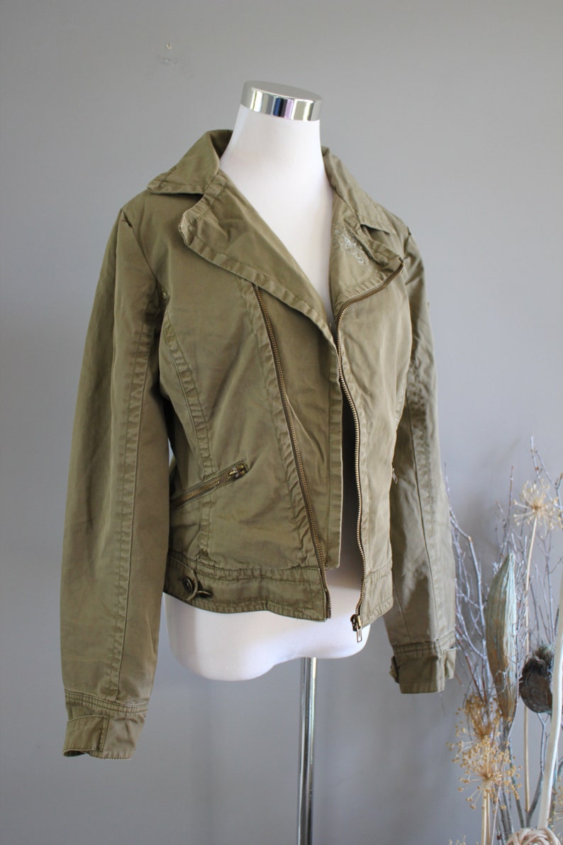 May include: A green zippered jacket with a collar and long sleeves. The jacket has a zipper closure and multiple pockets.