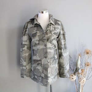 May include: A hooded camouflage jacket with a button-up front and multiple pockets.