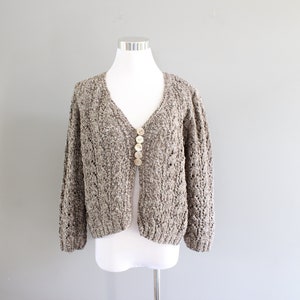 May include: A brown and white knit cardigan with a V-neck and button closure. The cardigan has a loose fit and a slightly cropped length.