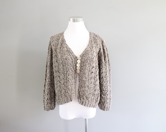 May include: A brown and white knit cardigan with a V-neck and button closure. The cardigan has a loose fit and a slightly cropped length.