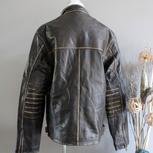 K&ouml;nnte beinhalten: Eine braune Lederjacke mit Rei&szlig;verschluss und Stehkragen. Die Jacke hat einen Used-Look mit hellbraunen N&auml;hten und einem Rei&szlig;verschluss an jedem &Auml;rmel.