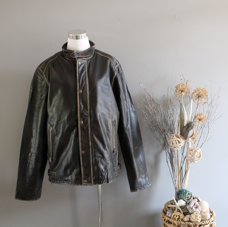 K&ouml;nnte beinhalten: Eine braune Lederjacke mit Rei&szlig;verschluss und Stehkragen. Die Jacke hat einen Used-Look und besticht durch N&auml;hte.