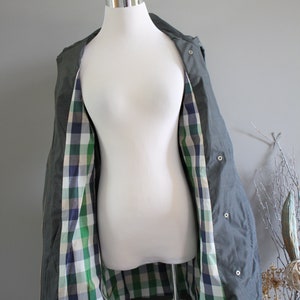 May include: A green hooded jacket with a plaid lining. The jacket is open and the lining is visible. The jacket is on a white mannequin.
