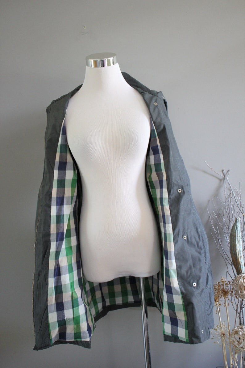 May include: A green hooded jacket with a plaid lining. The jacket is open and the lining is visible. The jacket is on a white mannequin.