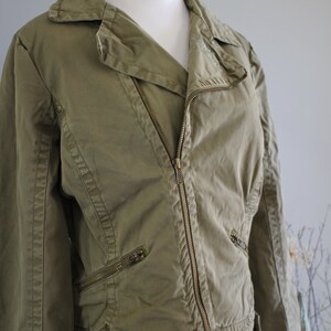 May include: A green cotton moto jacket with a zipper closure and multiple pockets. The jacket has a slightly cropped length and a relaxed fit.