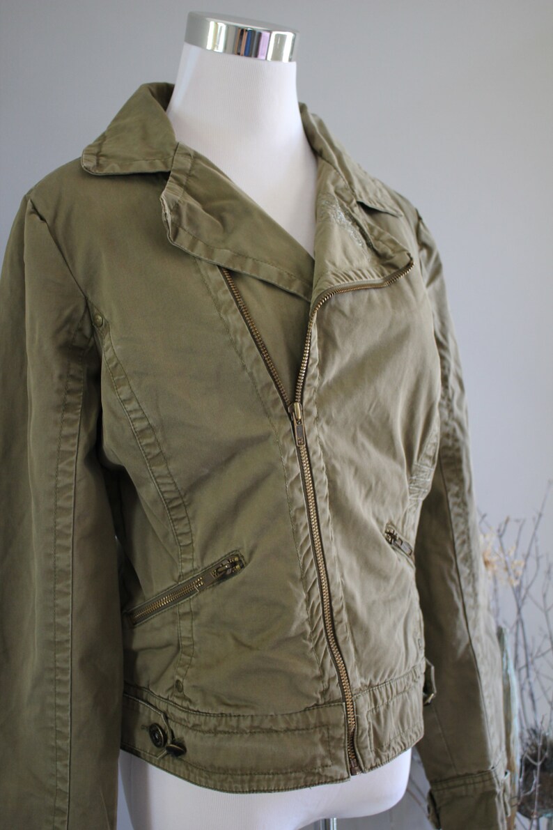 May include: A green cotton moto jacket with a zipper closure and multiple pockets. The jacket has a slightly cropped length and a relaxed fit.