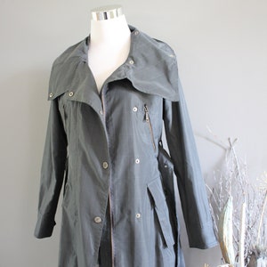 May include: A long, gray, collared jacket with a zipper and buttons. The jacket has a belt and pockets.